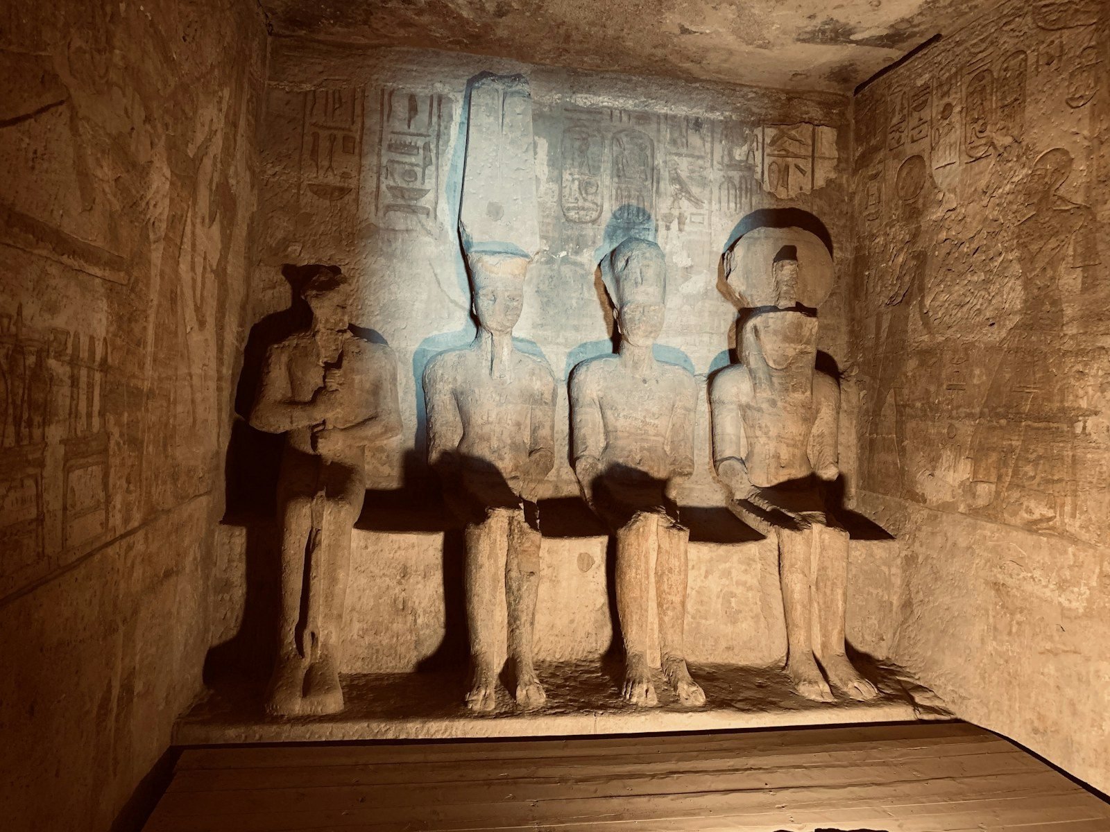 Cuatro estatuas sentadas en el santuario excavado en la roca del Gran Templo de Abu Simbel, iluminadas por un foco sobre un suelo de madera.