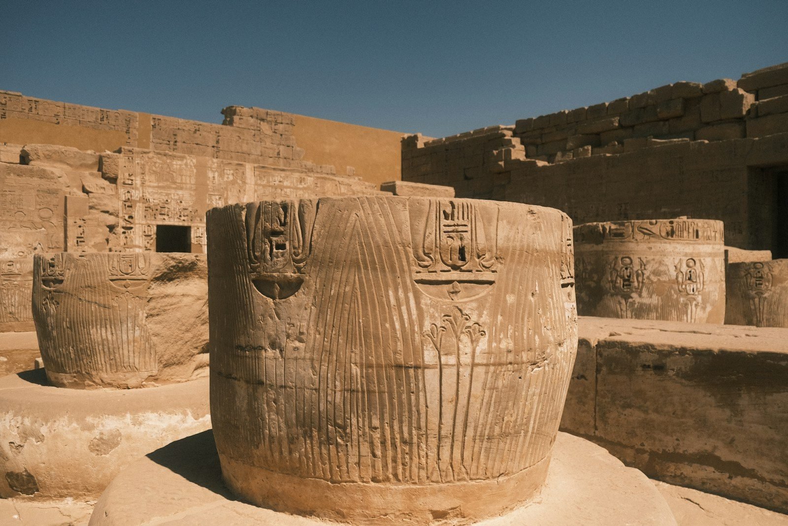 Tambores de columnas en forma de haces de papiro, tallados con cartuchos y jeroglíficos, en el patio en ruinas de un templo bajo un cielo azul intenso.