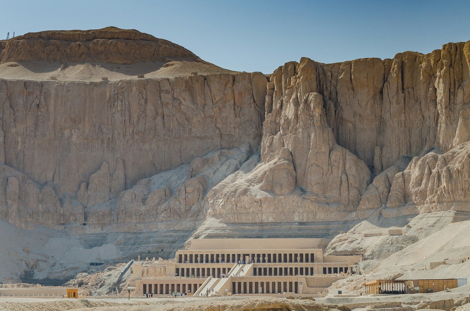 El templo de terrazas de Hatshepsut en Deir el Bahari al pie de un enorme acantilado de roca, con diminutos visitantes en las columnatas.